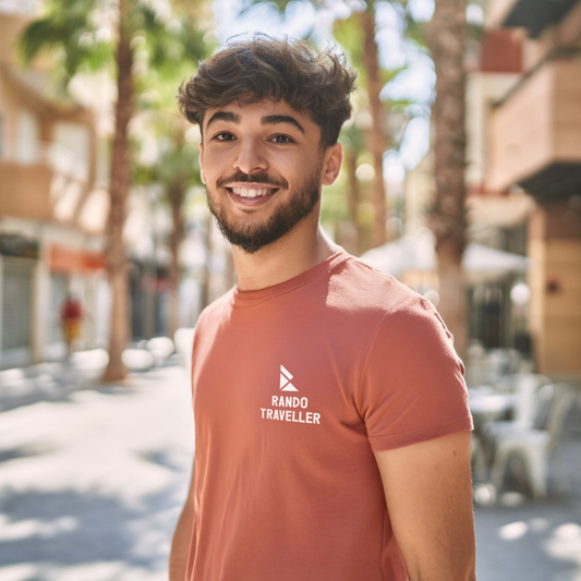 Man wearing a 'Rando Traveller' t-shirt standing outdoors with palm trees and buildings in the background.